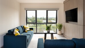 Un soggiorno moderno con un divano blu, una TV a schermo piatto montata a parete e un'ampia finestra con vista sull'esterno.