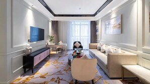 A modern hotel room with a large flat-screen TV, a sofa, a dining table, and a large window with curtains. - Count Diamond Hotel (Longli)
