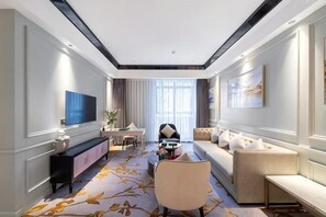 A modern hotel room with a large flat-screen TV, a sofa, a dining table, and a large window with curtains. - Count Diamond Hotel (Longli)
