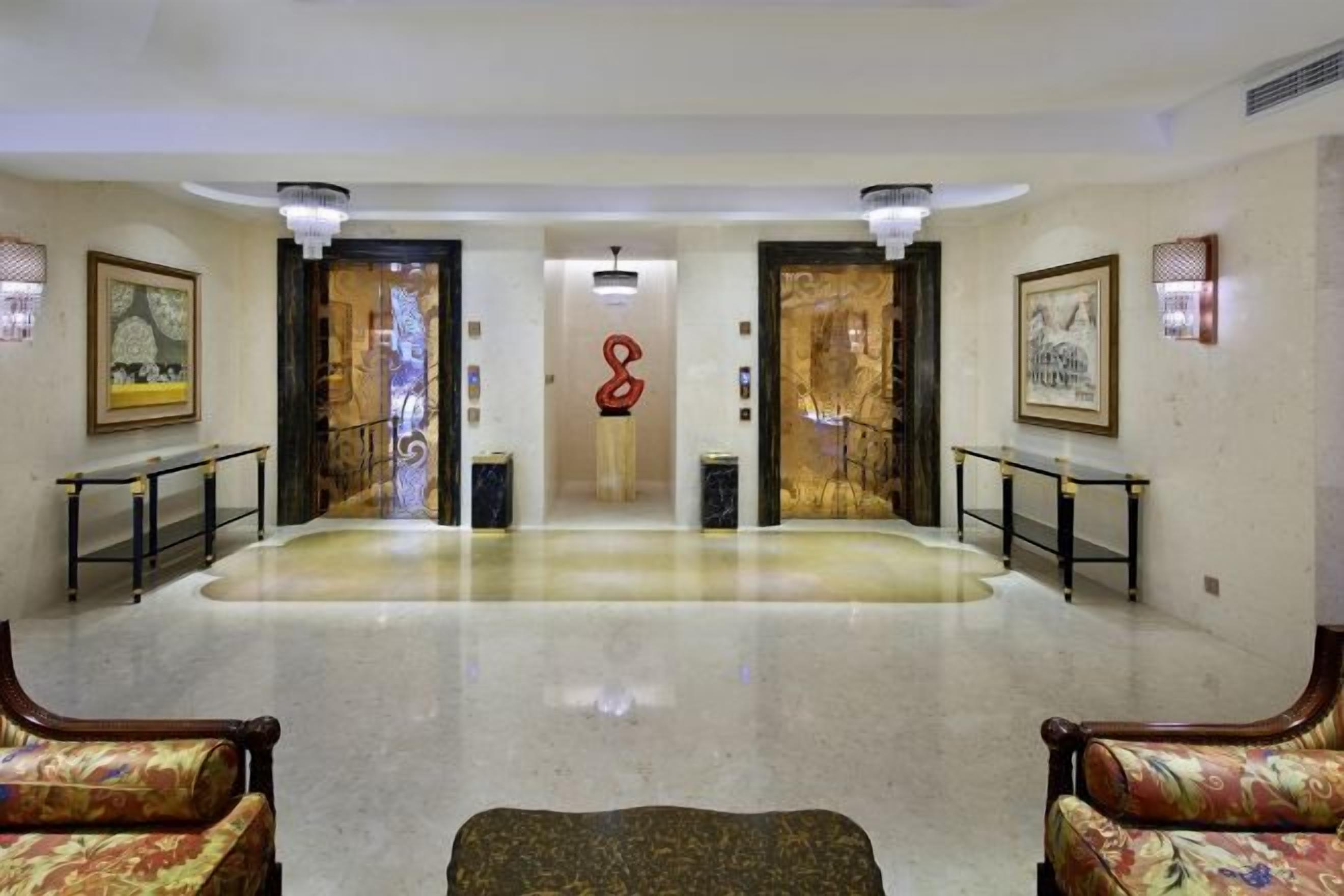 A hotel lobby with a polished floor, two doors, and a central red sculpture.