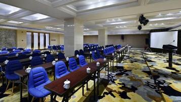 Un salón de conferencias con hileras de sillas azules, una larga mesa con micrófonos y un escenario con un atril.