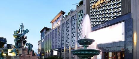 La façade d’un hôtel, avec un grand écran numérique, une fontaine et une statue au premier plan.
