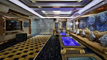 Een luxueuze kamer met een zwart-wit betegelde vloer, een centraal gelegen verwarmd zwembad, comfortabele zitplaatsen en een grote televisie.