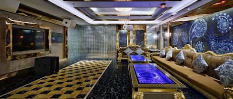 Una habitación lujosa con piso de cuadros, piscina central climatizada, asientos cómodos y un televisor grande.