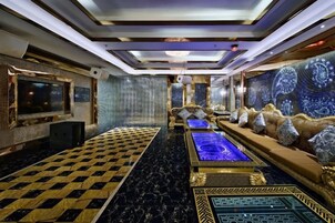 Quarto luxuoso com piso xadrez, piscina central aquecida, assentos confortáveis e uma televisão grande.