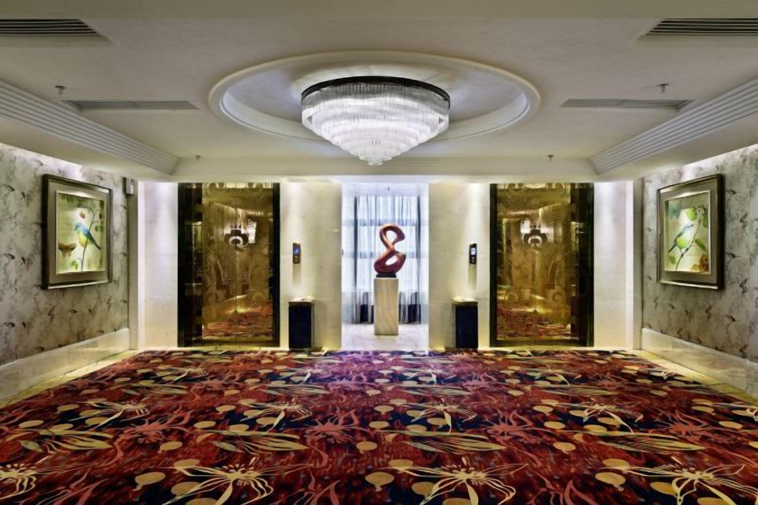 A spacious room with a large carpet, a chandelier, and framed artwork on the walls.