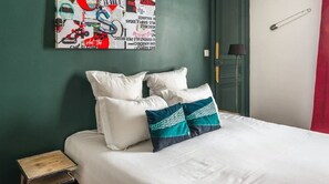 A neatly made bed with white and teal pillows, a wooden nightstand, and a wall with a colorful abstract artwork.