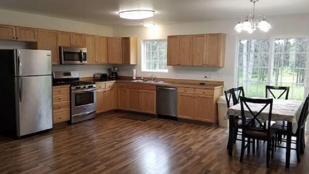 A kitchen with wooden cabinets, stainless steel appliances, and a dining area with a table and chairs.