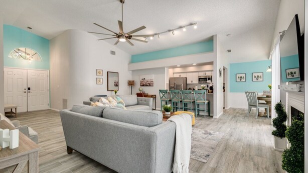 A modern living room with a grey sofa, a ceiling fan, and a dining area with green chairs. - Palm harbor/Crystal Beach 3/2 W Heated pool & Spa (Palm Harbor)