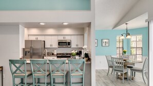 A modern kitchen with white cabinets, stainless steel appliances, and teal chairs. - Palm harbor/Crystal Beach 3/2 W Heated pool & Spa (Palm Harbor)