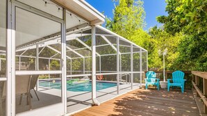 A screened-in outdoor area with a pool, wooden deck, and two blue Adirondack chairs. - Palm harbor/Crystal Beach 3/2 W Heated pool & Spa (Palm Harbor)