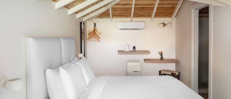 Un dormitorio con techo alto de madera, cama con ropa blanca, mesita de noche, pequeña lámpara de noche, aire acondicionado instalado en la pared y estante de madera con un jarrón.