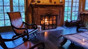 A cozy cabin interior with a fireplace, wooden beams, and large windows.