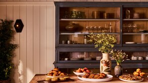 A wooden ceiling with exposed beams, a kitchen counter with pastries, and a cabinet with glassware.
