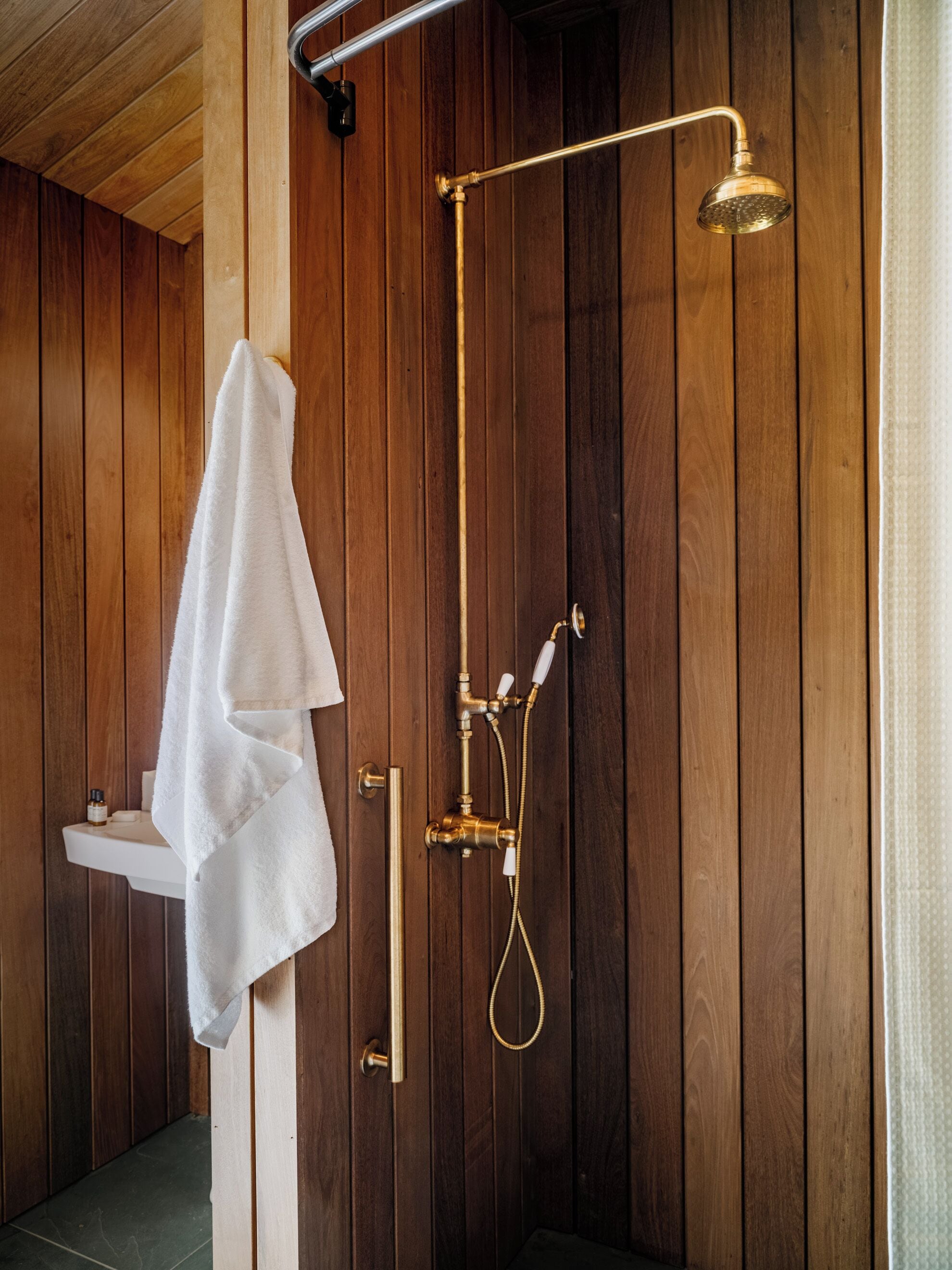 A wooden-paneled bathroom with a gold shower fixture, a white sink, and a towel hanging on the door.
