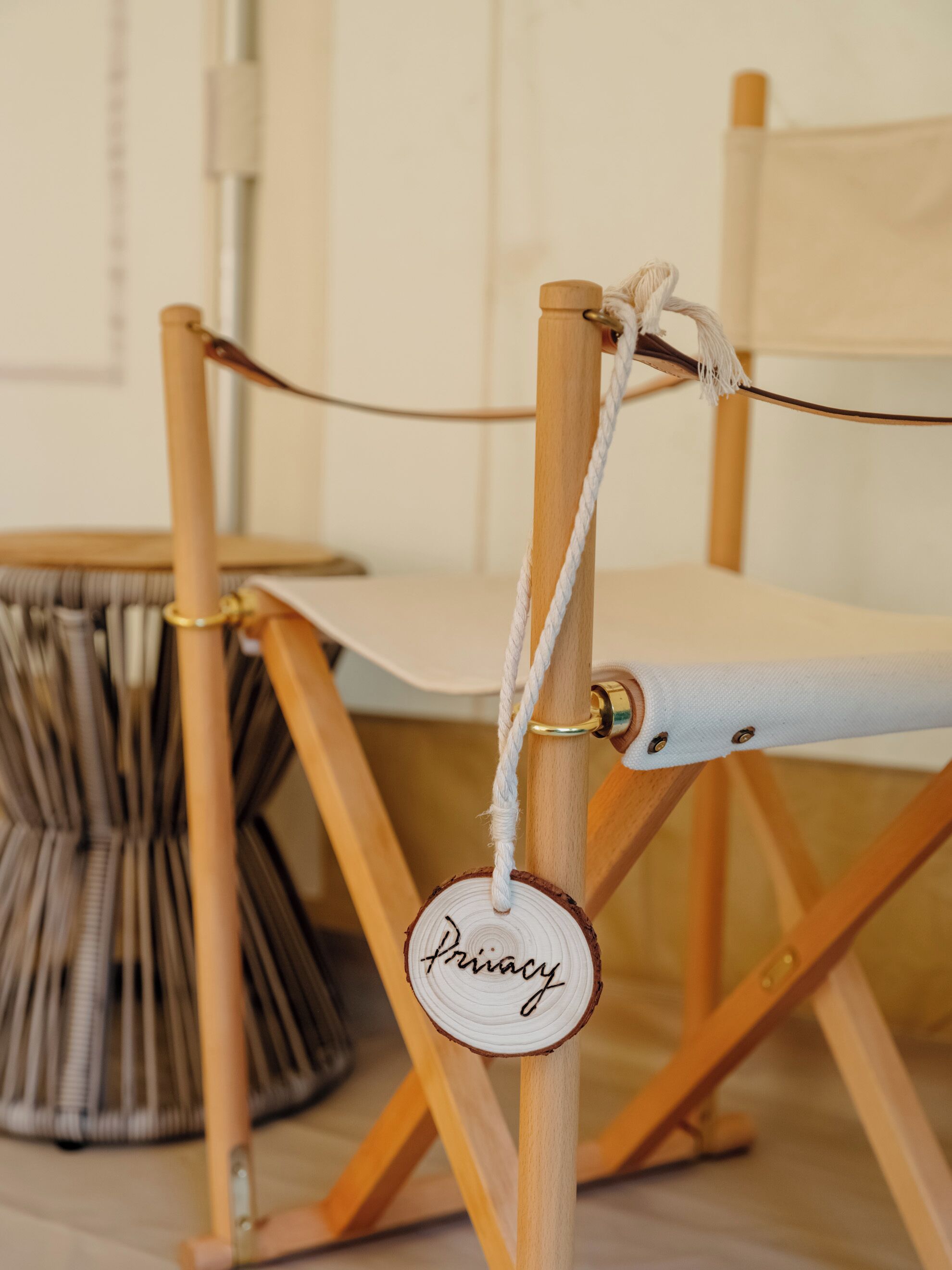 Una sedia di legno con seduta e schienale in tela, legata a un palo di legno con una corda. Una targa rotonda di legno con la scritta 'Privacy' è fissata al palo.