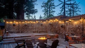 An outdoor patio with wooden decking, fire pit, seating, and string lights.