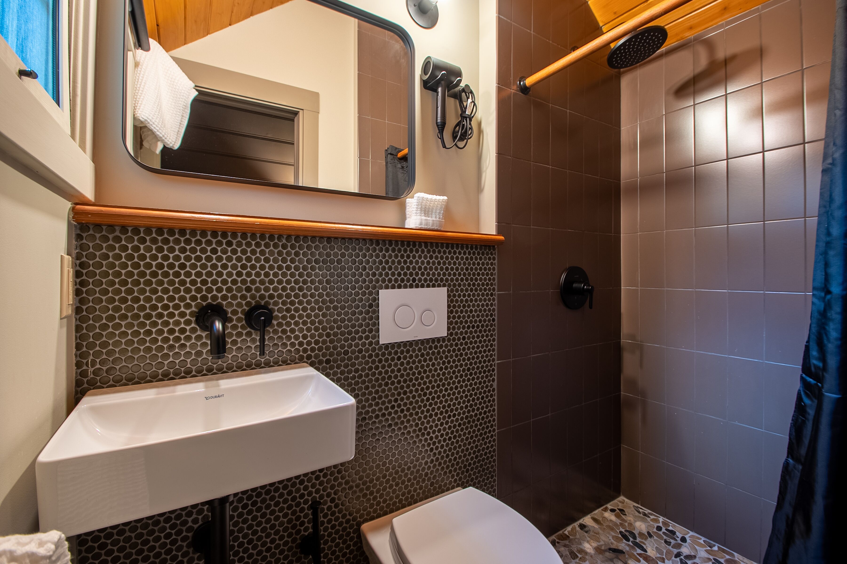 A bathroom with a sink, mirror, towel rack, and shower area.