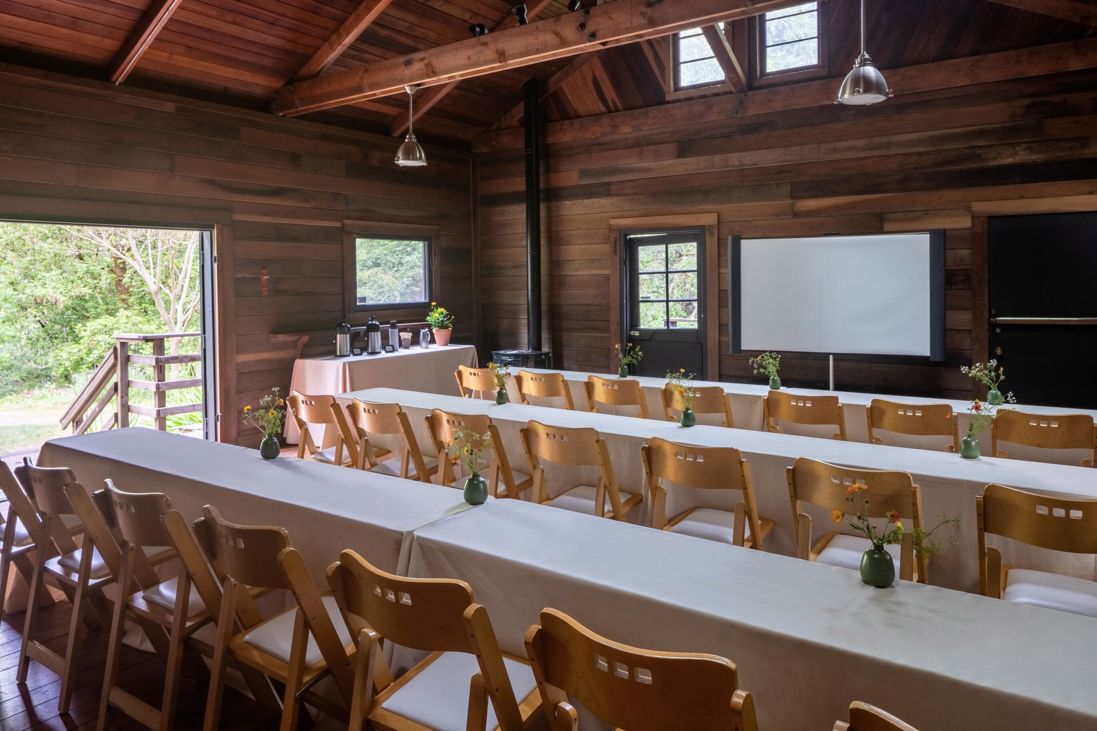 A long dining table with chairs, wooden walls, and a projector screen.