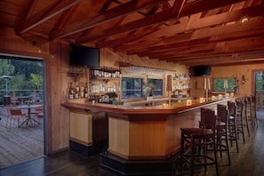 A wooden bar area with a counter, bar stools, and a television mounted above.