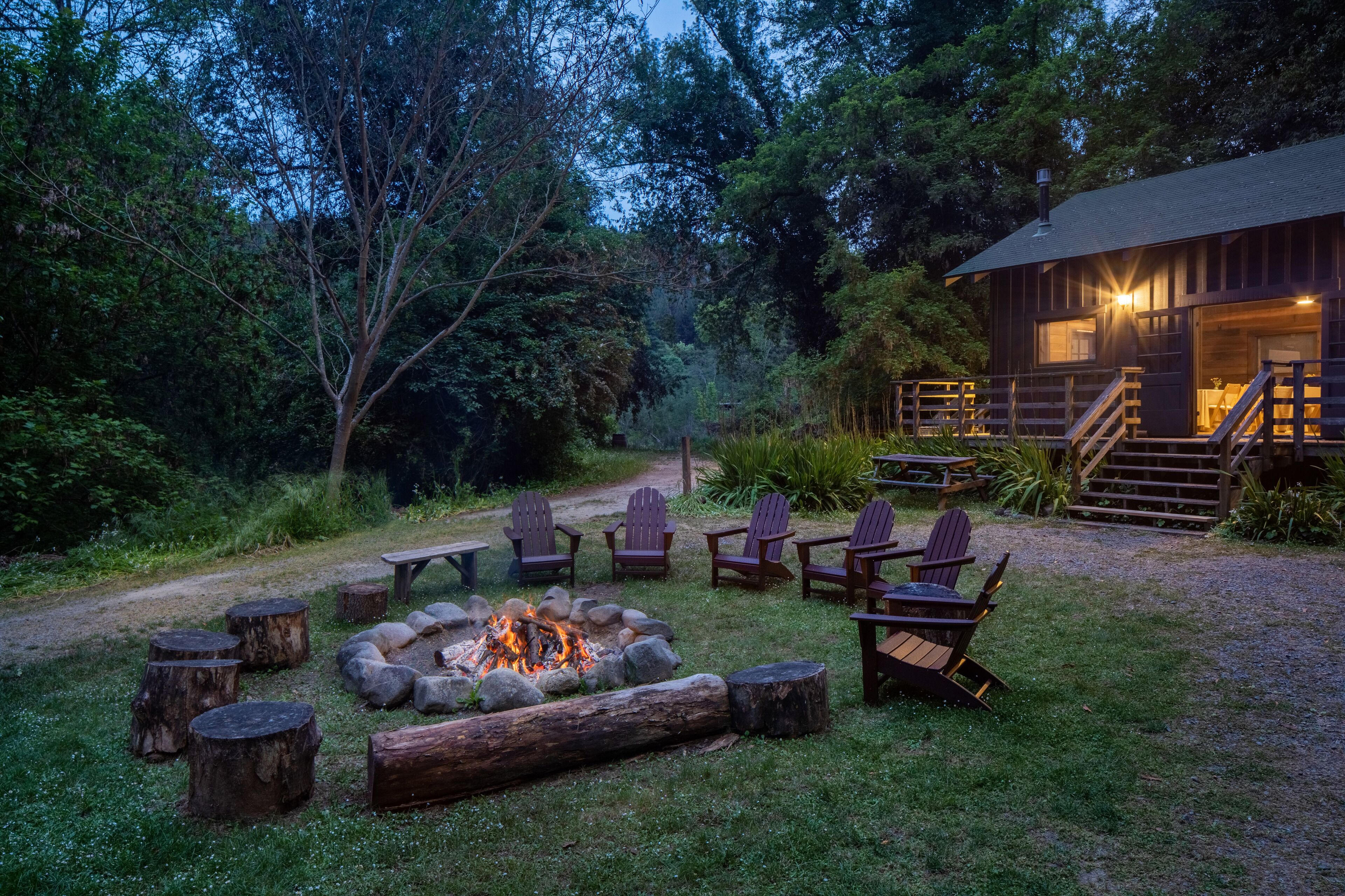 Eine rustikale Holzhütte mit Feuerstelle und Adirondack-Stühlen in bewaldeter Landschaft.