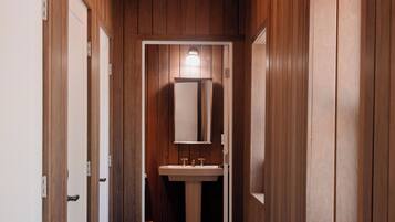 A hallway with wooden walls and doors, leading to a bathroom with a sink and mirror.