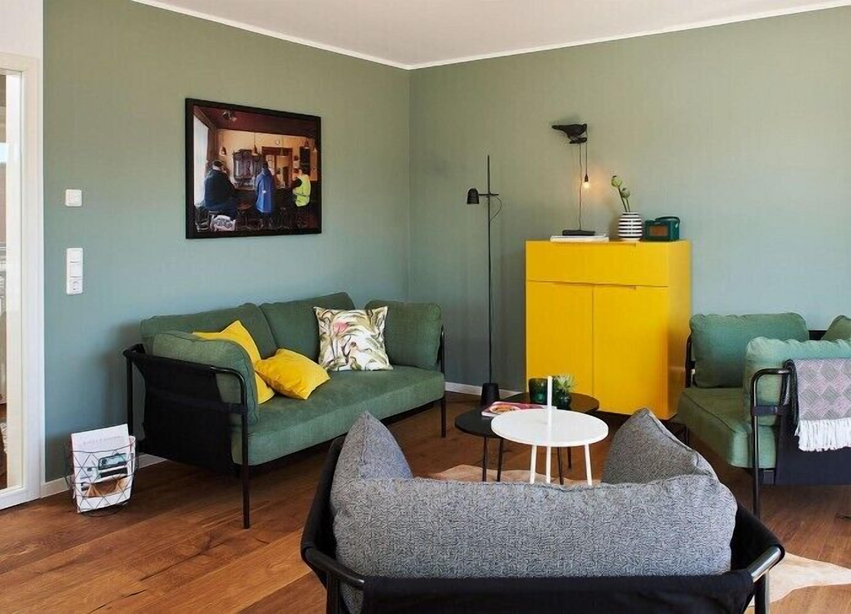 A living room with a green sofa, a yellow cabinet, and a gray armchair.