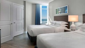 A hotel room with two beds, a nightstand with a lamp, a painting on the wall, and a view of the ocean through a window. - Luxury 2 Bedroom unit in beachfront Myrtle Beach resort Sleeps 8 (Myrtle Beach)