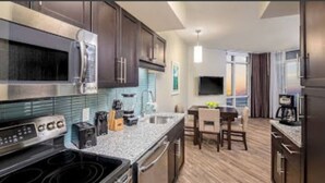 A modern kitchen with stainless steel appliances, a granite countertop, and a dining area with a table and chairs. - Luxury 2 Bedroom unit in beachfront Myrtle Beach resort Sleeps 8 (Myrtle Beach)