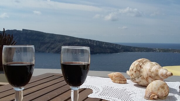 Deux verres de vin rouge sur une table en bois, avec une vue sur la mer et les montagnes en arrière-plan.