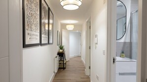 A hallway with framed artwork, a table with a plant, and a bathroom visible through an open door. - Courtyard View (Southampton)
