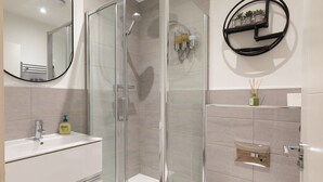 A modern bathroom with a glass-enclosed shower, a white sink with a mirror, and a toilet. - Courtyard View (Southampton)