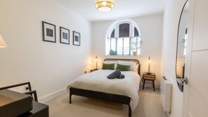 A bedroom with a bed, bedside lamps, a window with a view, and framed pictures on the wall. - Courtyard View (Southampton)