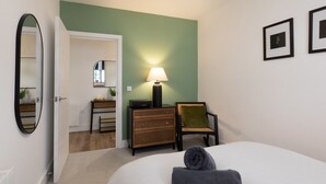A bedroom with a bed, a dresser, a chair, a lamp, and a mirror. - Courtyard View (Southampton)