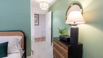 Une chambre à coucher avec un lit, une commode, une lampe et une porte donnant sur une autre pièce.