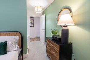 Un dormitorio con cama, cómoda, lámpara y puerta que da a otra habitación.
