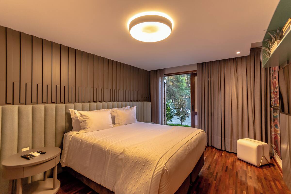 Una camera d'albergo moderna con un letto grande, un comodino, un piccolo angolo salotto e vista sull'esterno.