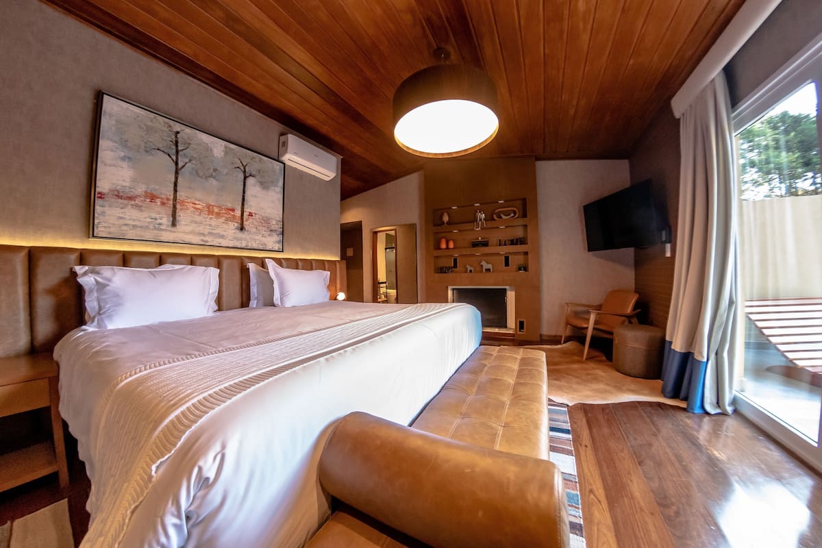 Una camera da letto con un letto grande, una panca, un camino, una televisione e una finestra con tende.
