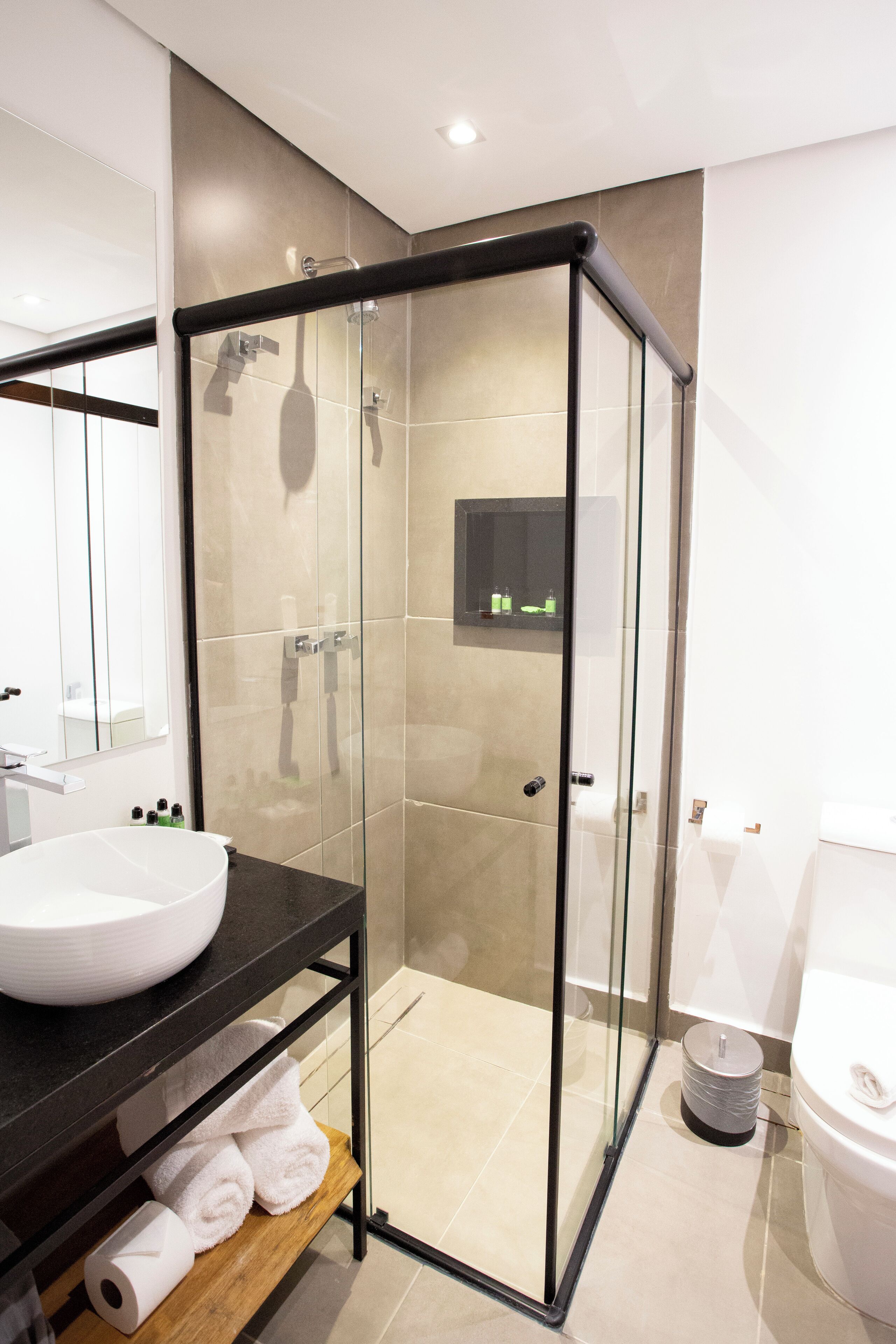 Un bagno moderno con doccia vetrata, un piano d'appoggio nero con lavandino bianco e una mensola in legno con asciugamani.