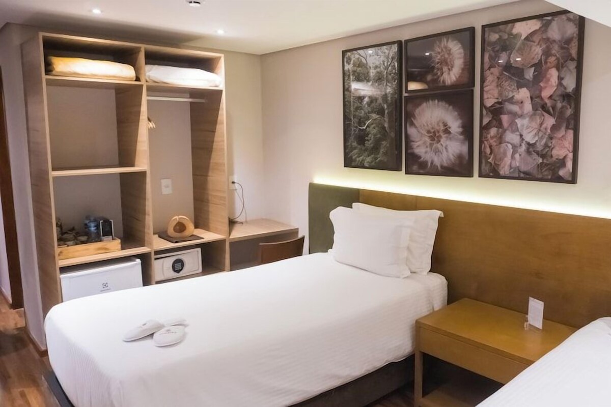 Habitación de hotel con cama, mesitas de noche, armario y cuadros en la pared.