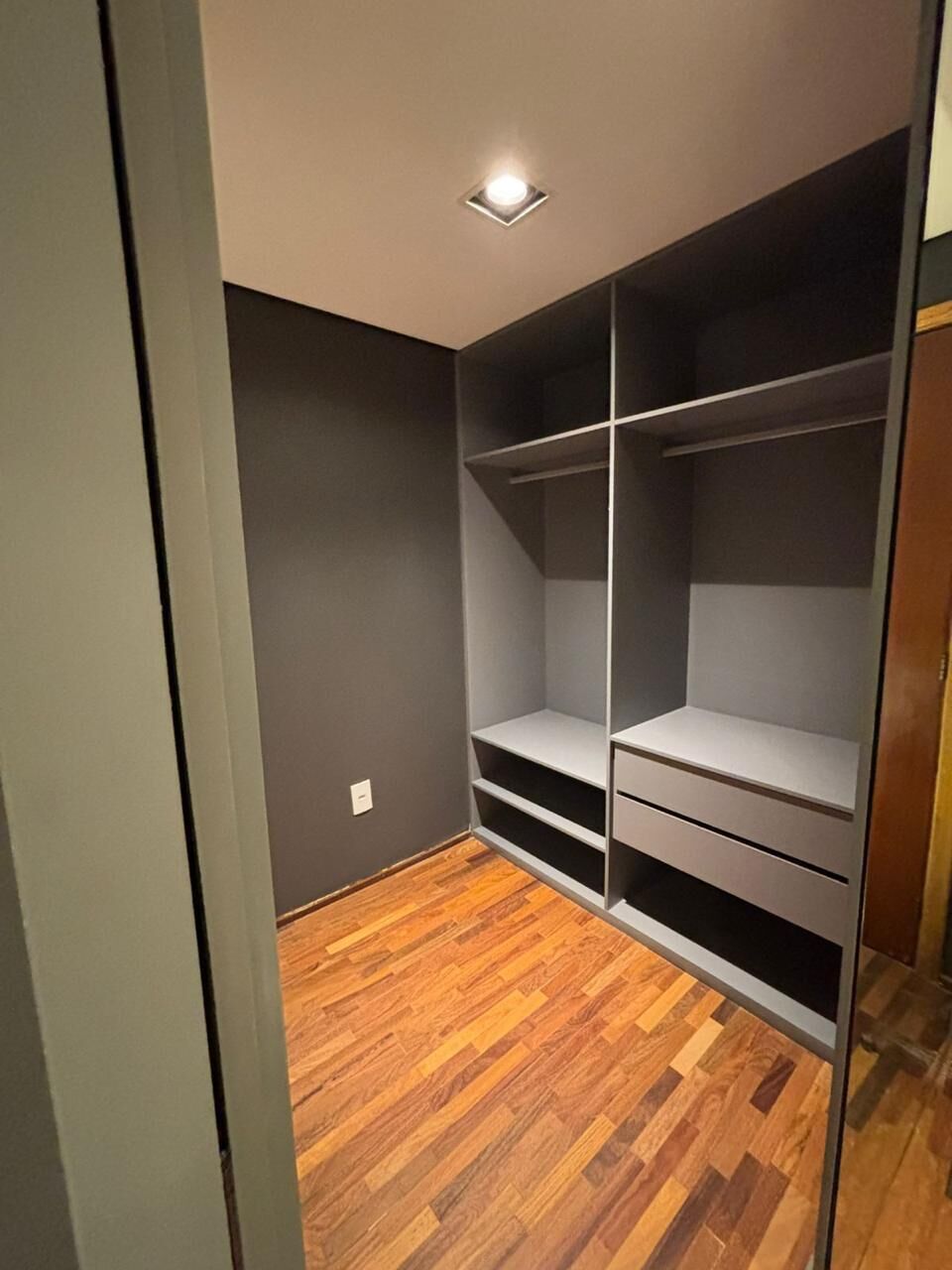 Um closet espaçoso com prateleiras abertas e gavetas, piso de madeira e iluminação embutida no teto.