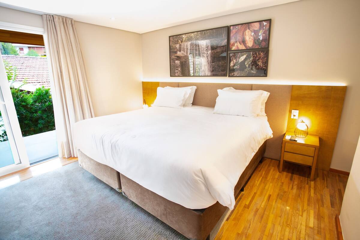 Camera d'albergo con un letto grande, un comodino con una lampada, una porta scorrevole in vetro e un'opera d'arte appesa al muro.
