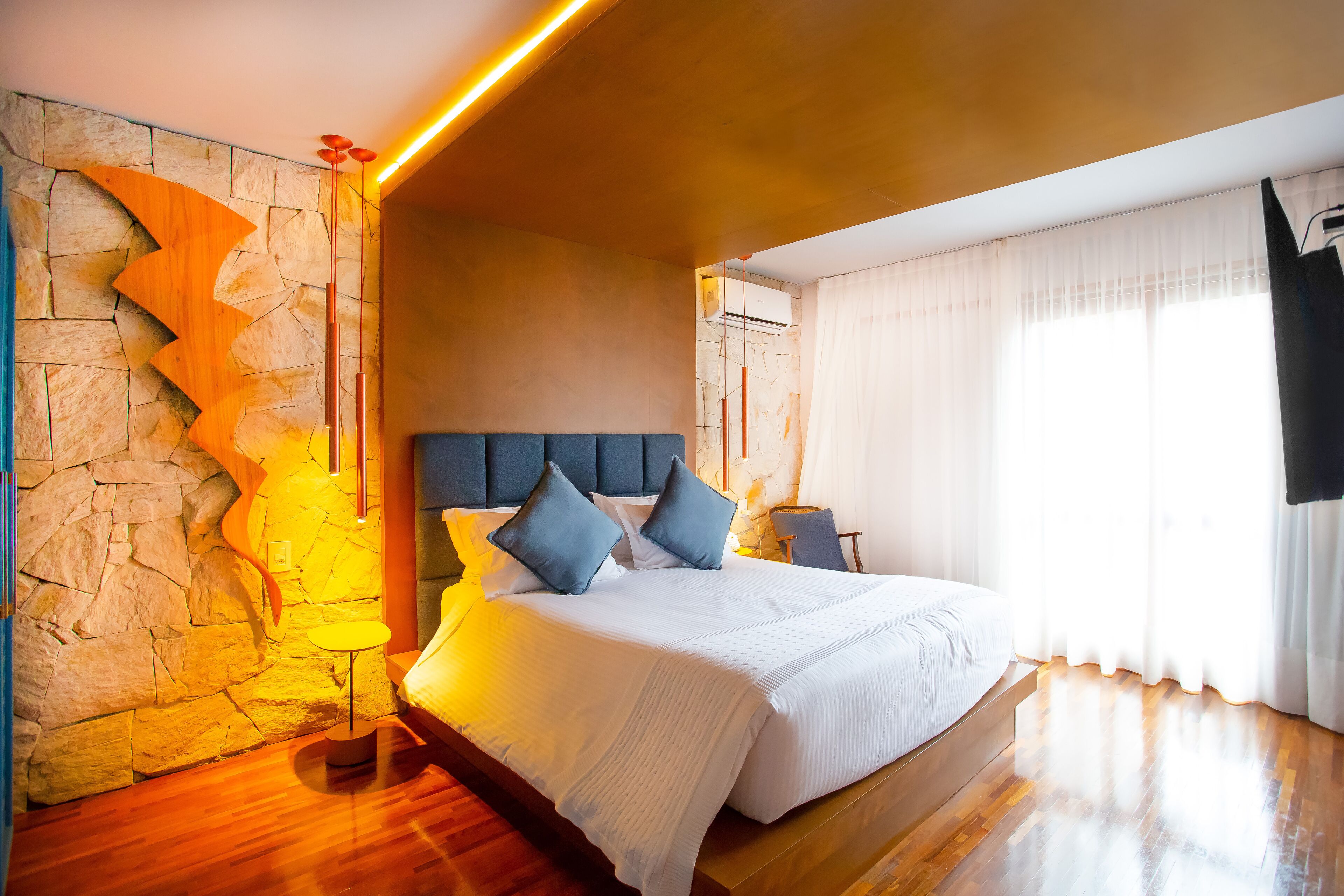 A modern bedroom with a stone accent wall, a large bed with blue pillows, and a wooden floor.