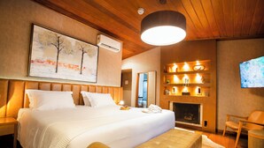 Ein modernes Hotelzimmer mit einem großen Bett, einem Kamin, einem Fernseher und einer Holzbalkendecke.