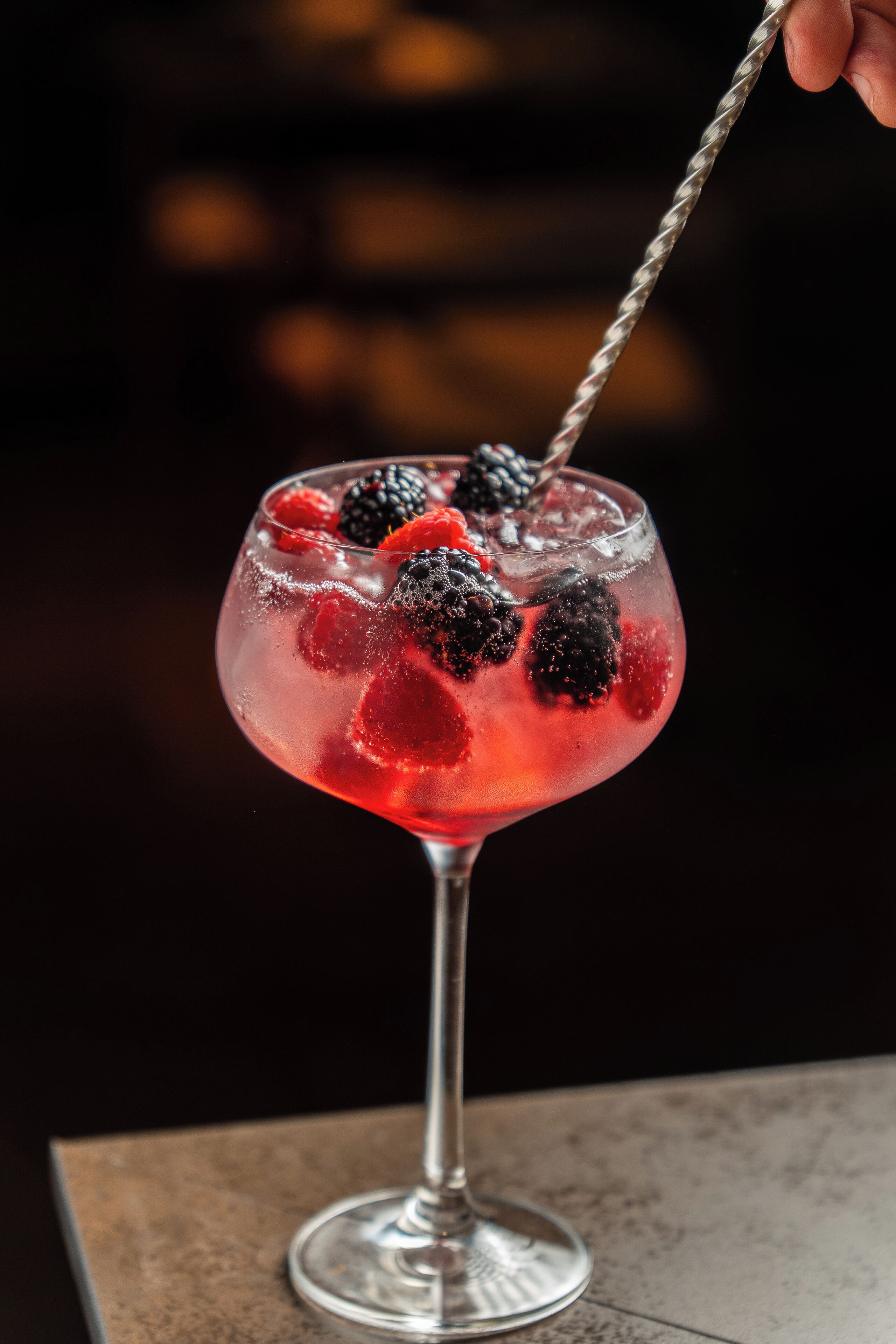 Een cocktailglas met ijs en bessen op een tafel.