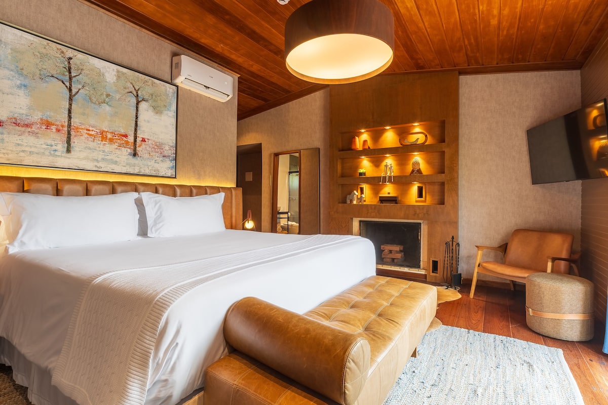 Una moderna camera d'hotel con un grande letto, una testiera in legno, una TV a parete, un caminetto e un'accogliente area salotto.