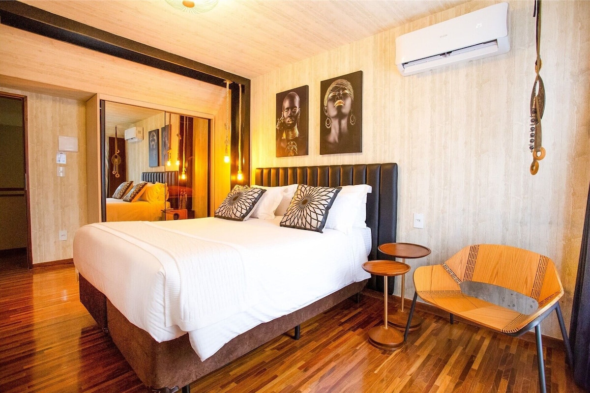 Una camera d'albergo con un letto, una sedia, uno specchio e opere d'arte alle pareti.