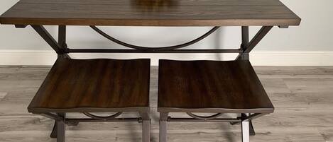 A square wooden table with two benches, a bowl of yellow objects on top, and metal legs.