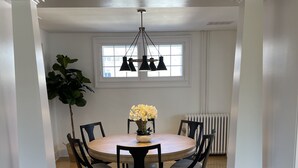 Een eetkamer met een ronde tafel, zwarte stoelen, een kroonluchter en een potplant.