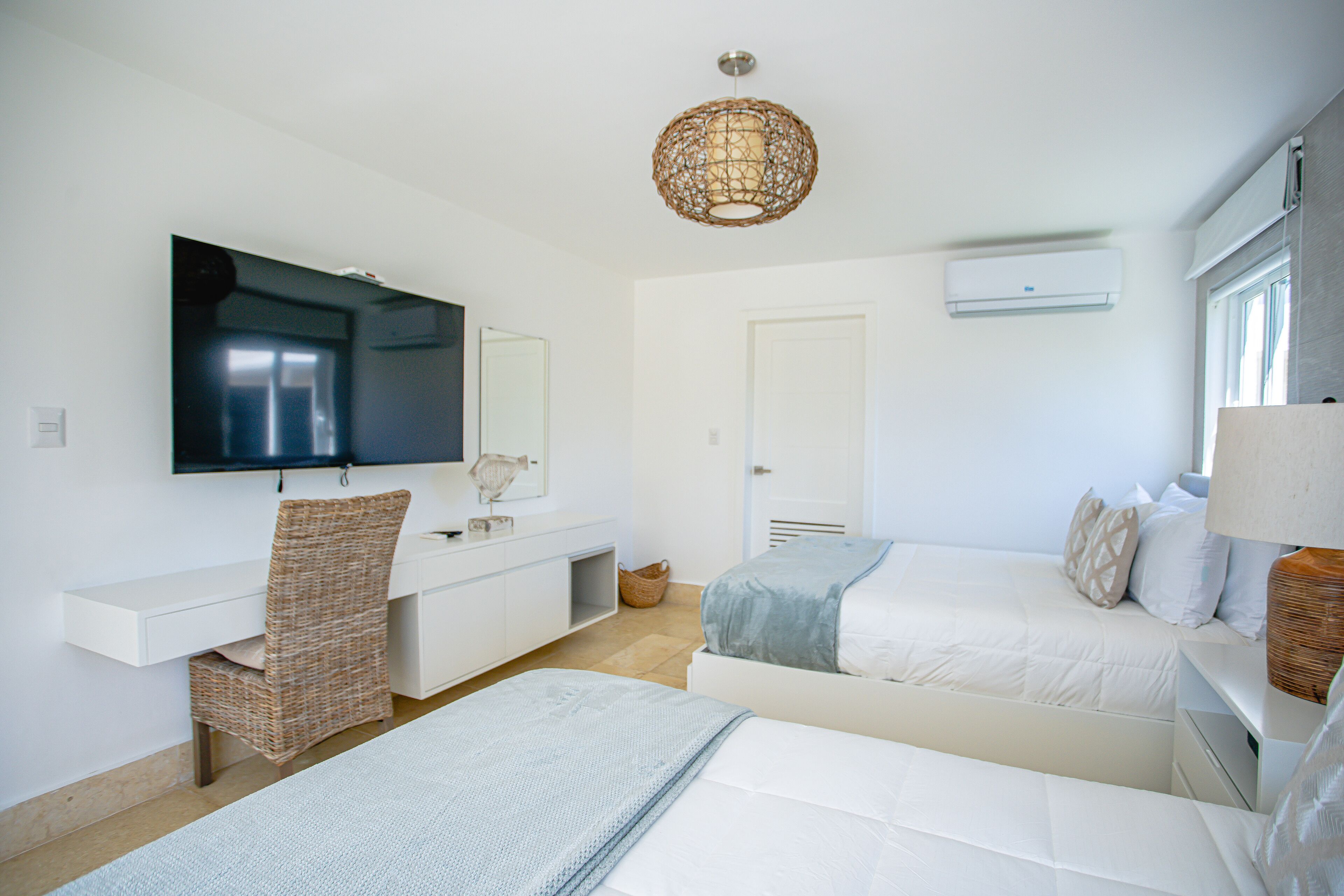 A bedroom with two beds, a desk, a chair, a television, and a ceiling light fixture.